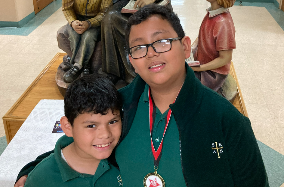 Foto de dos niños. El más alto lleva gafas y una medalla de "Rising Stars".